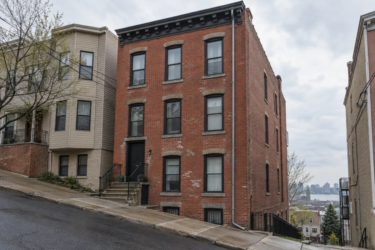 Three-story brick multifamily building on a sloped Union City street with a long leader running down the front