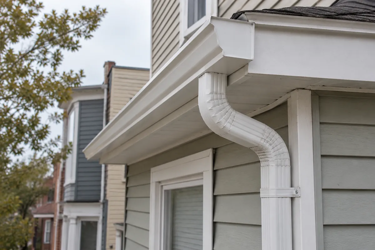 New white K-style gutter and leader on the side of a Jersey City frame two-family house